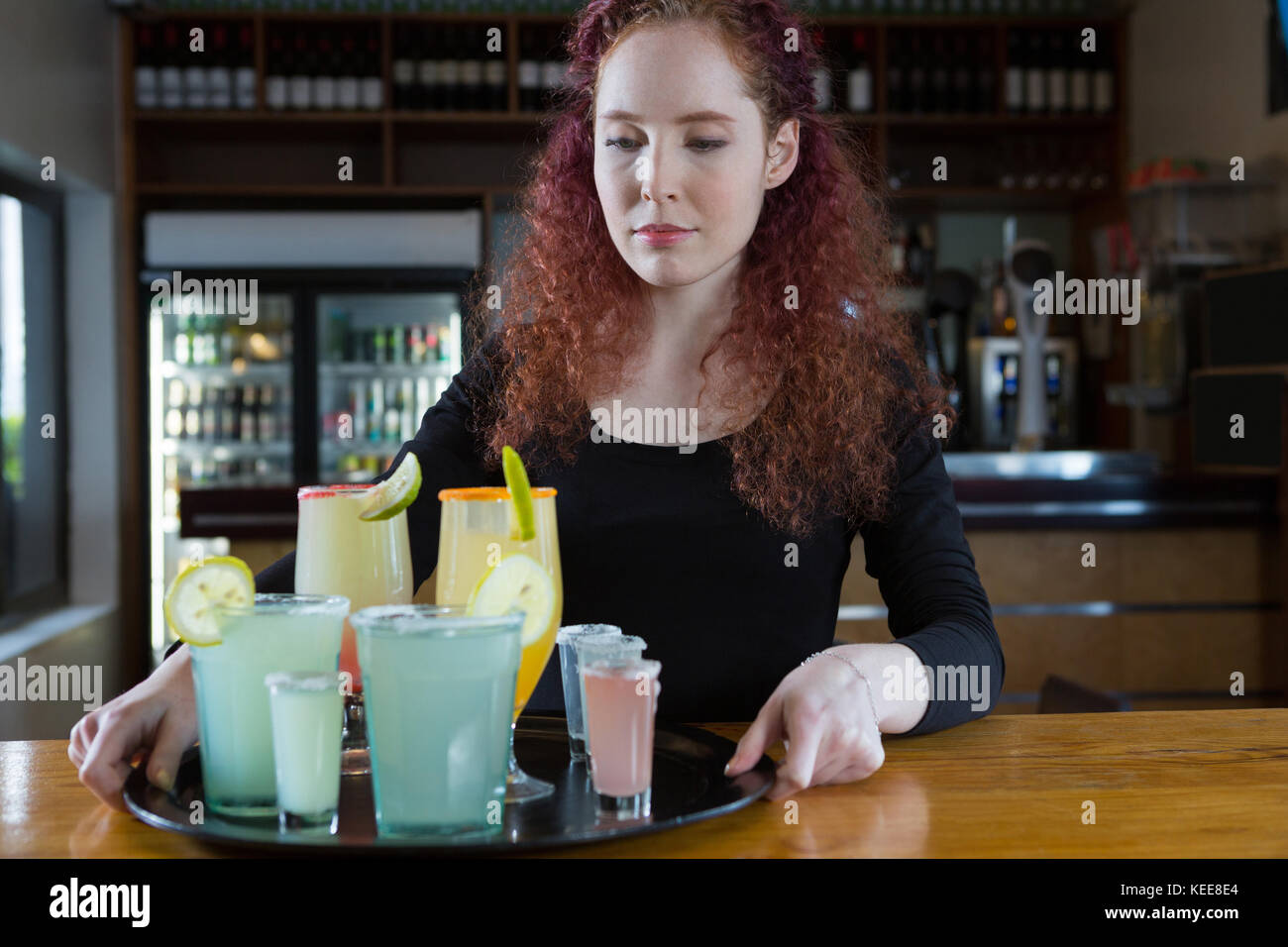 Beautiful waitress holding drinks near bar counter Stock Photo