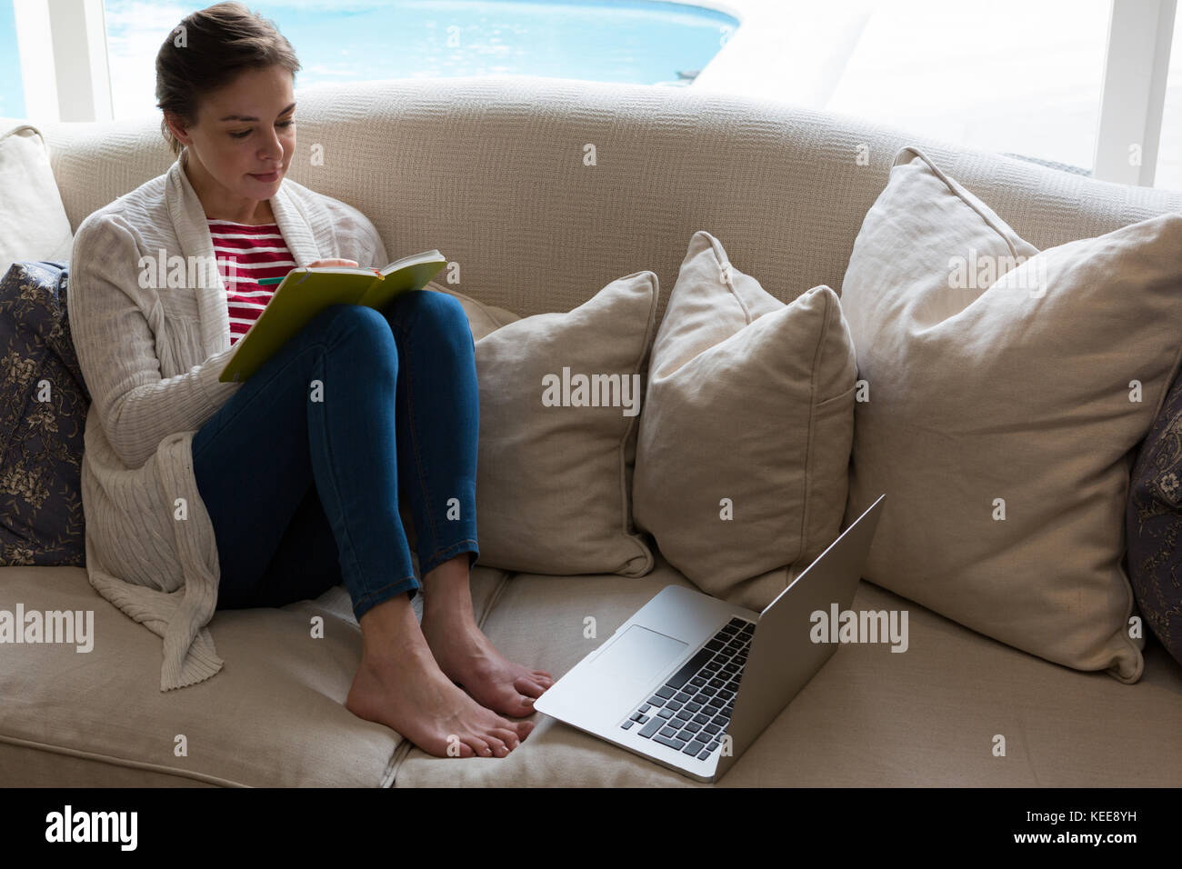 Woman reading book on sofa in living room Stock Photo - Alamy