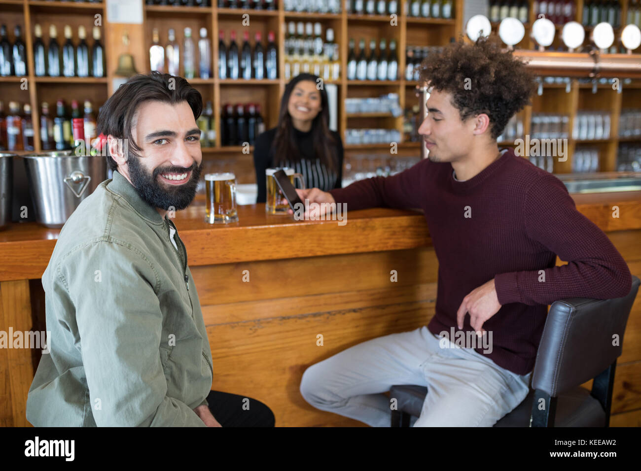 Waitress standing at counter while two men using mobile phone in bar Stock Photo