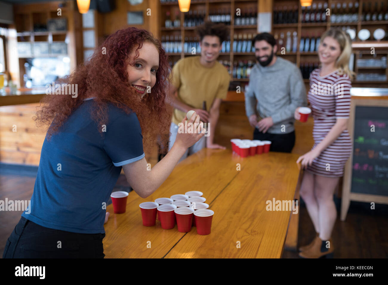 Portrait of smiling woman playing beer pong game with friends in bar