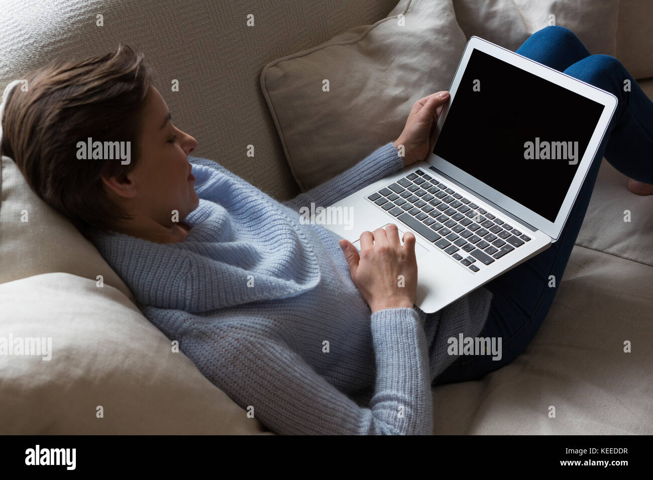 Woman using laptop while relaxing on sofa in living room Stock Photo ...