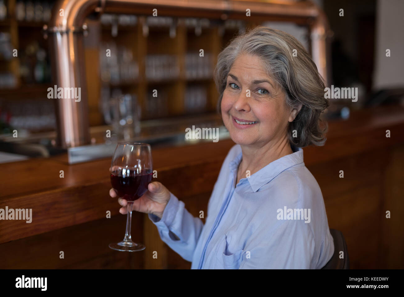 Portrait of smiling senior woman having glass of red wine at counter in ...