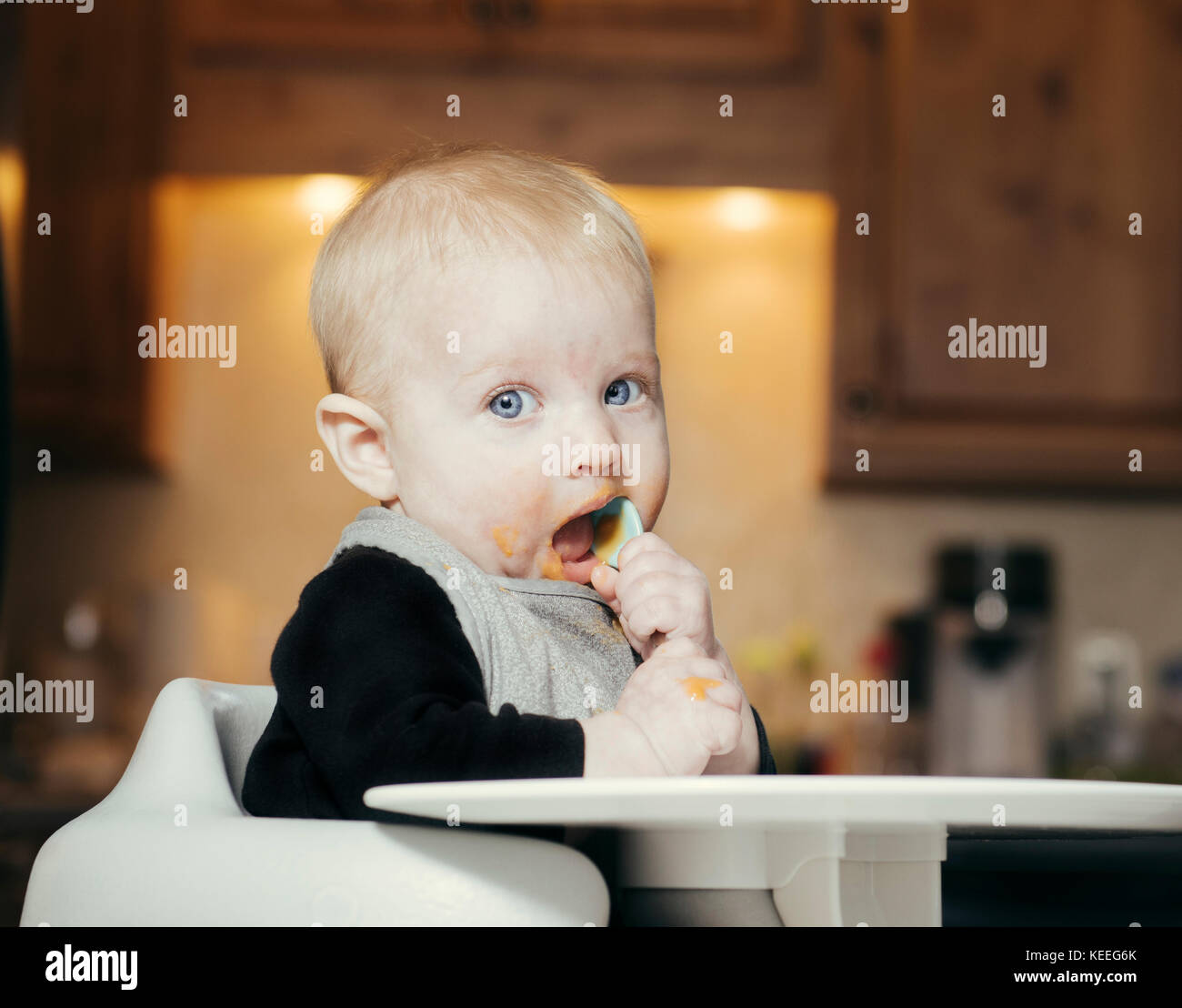 Baby Sitting in Highchair All Messy Eating Orange Baby Food with Spoon in Mouth Stock Photo Alamy