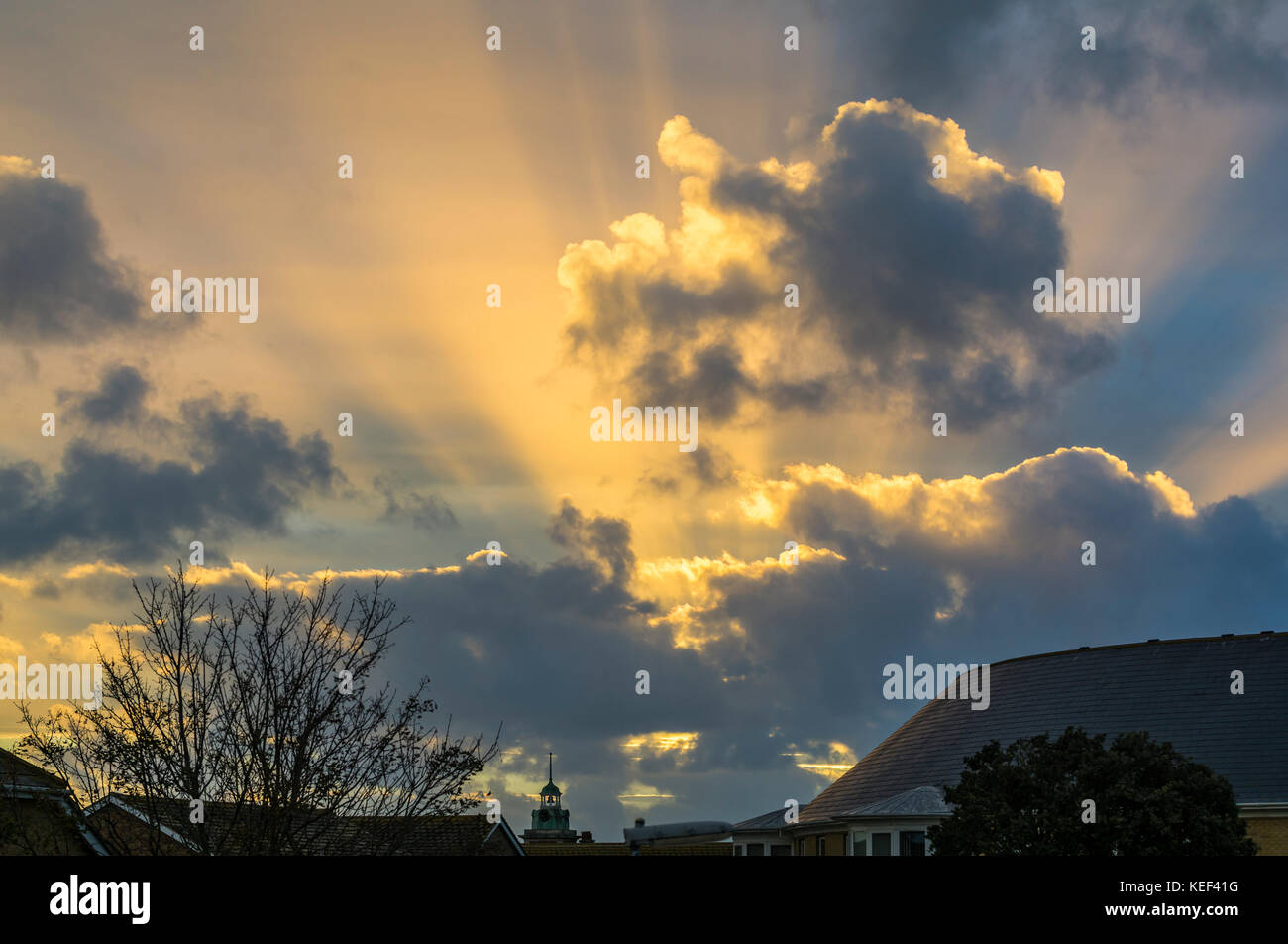 Sun going down behind clouds with suns rays visible on a cloudy evening. Stock Photo
