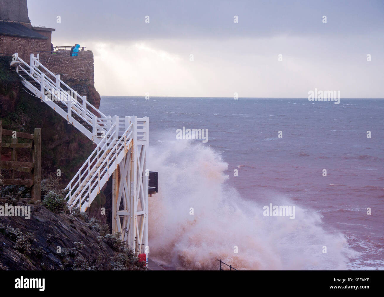 Sidmouth, UK. 21st Oct 2017. UK Weather. A couple view from high above as waves crash into Jacob's Ladder as Storm Brian pounds into Sidmouth, Devon. In stormy weather, the red sandstone of the area turns the sea red at Sidmouth. Credit: Photo Central/Alamy Live News Stock Photo