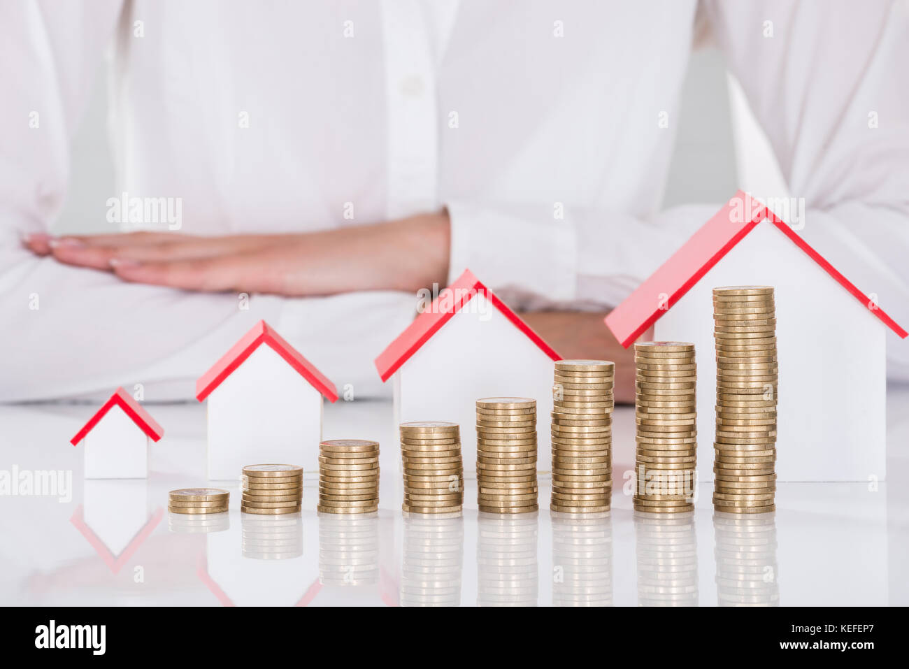 Close-up Of Businesswoman In Front Of Stacked Coins And House Models On Desk Stock Photo