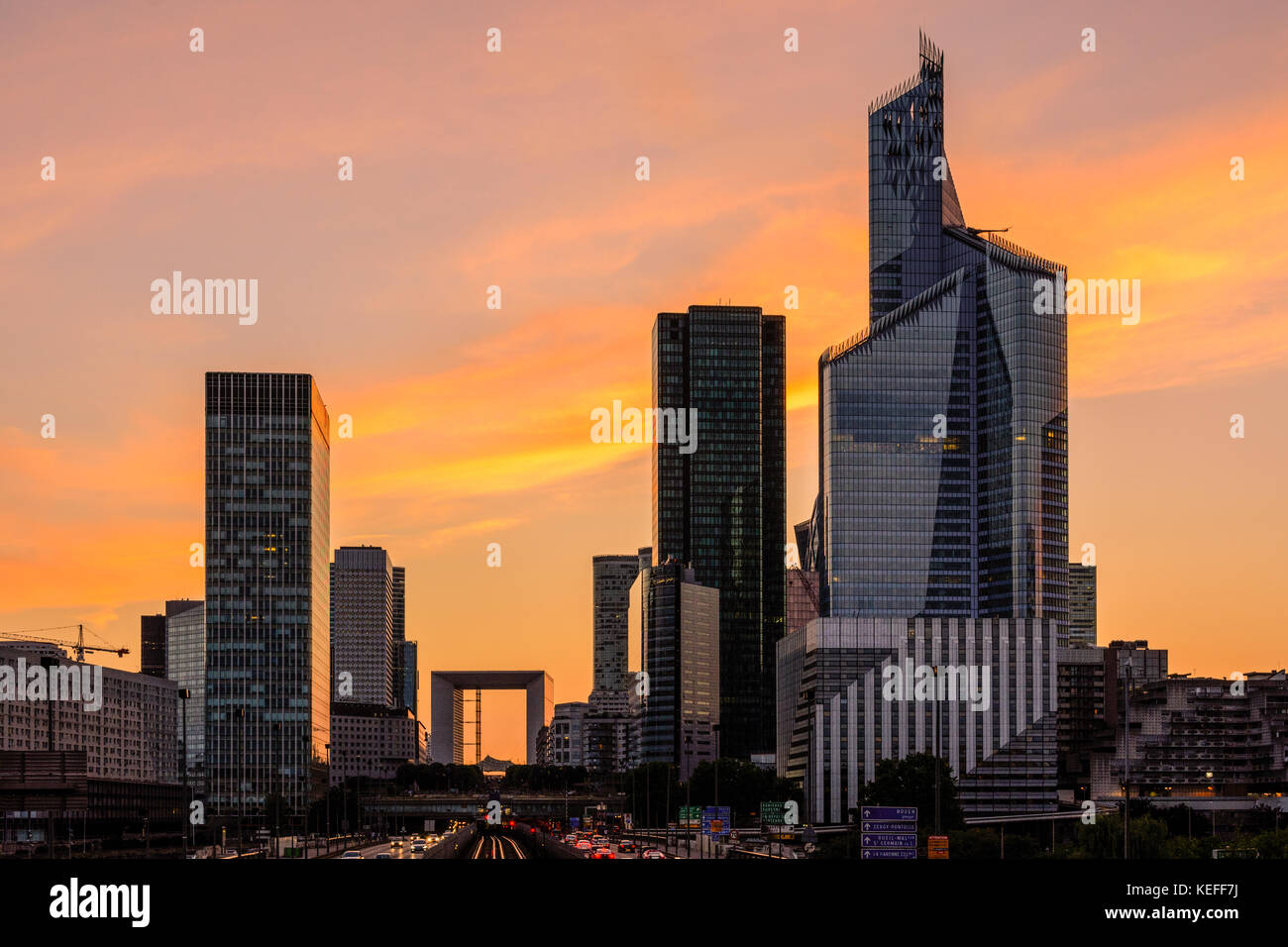 Skyline of Paris La Defense business district with the Grande Arche standing out against a glowing red sky. Stock Photo