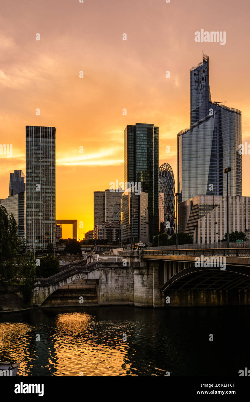 Skyline of Paris La Defense business district with the Grande Arche standing out against a glowing red sky and the Neuilly bridge in the foreground. Stock Photo