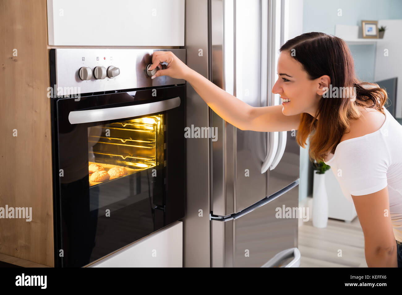 Young Woman Using Microwave Oven For Baking Fresh Cookies In Kitchen