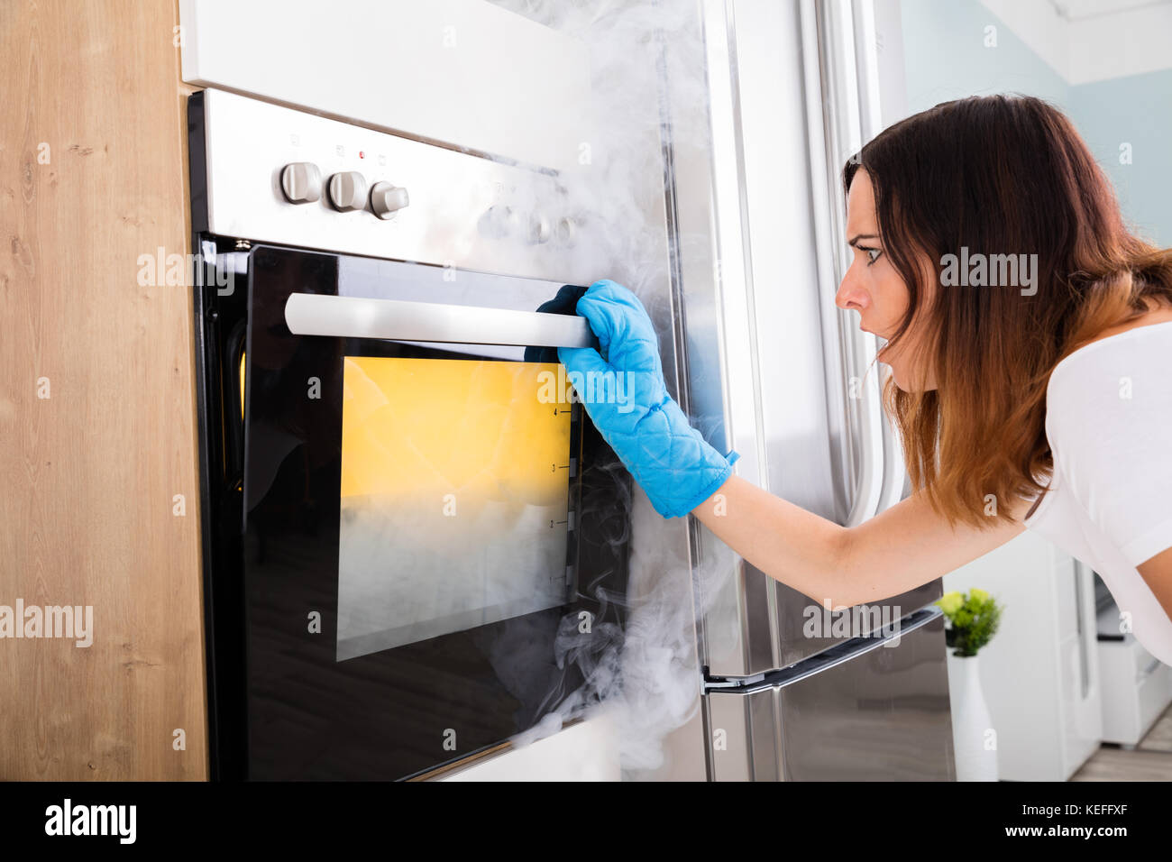 Shocked Young Woman Looking At Smoke Coming Out Of Oven In Kitchen