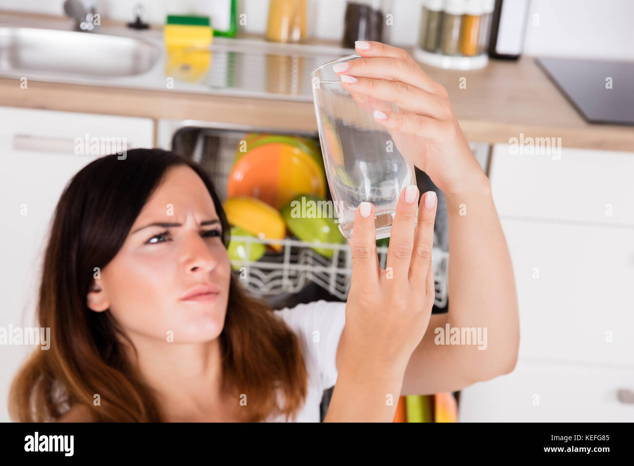 High Angle View Of Young Woman Looking At Clean Glass In Kitchen Stock Photo