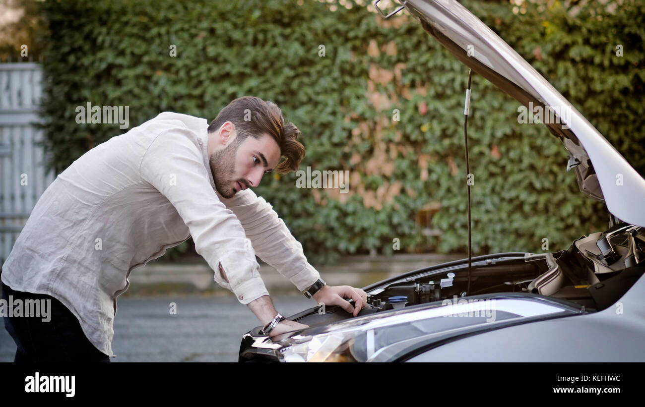 Handsome young man trying to repair a car engine, looking inside open ...