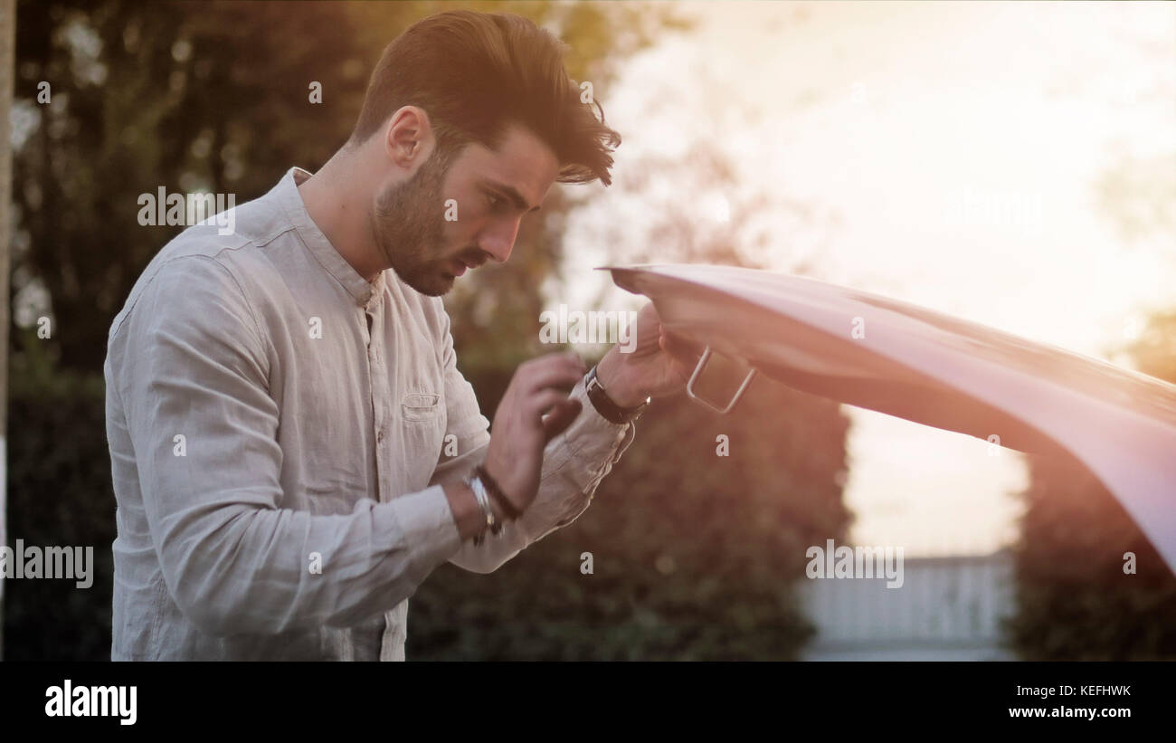 Handsome young man trying to repair a car engine, looking inside open ...
