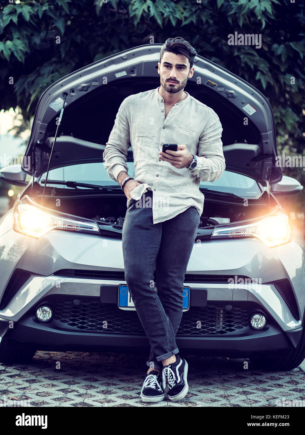 Handsome young man trying to repair a car engine, looking inside open ...
