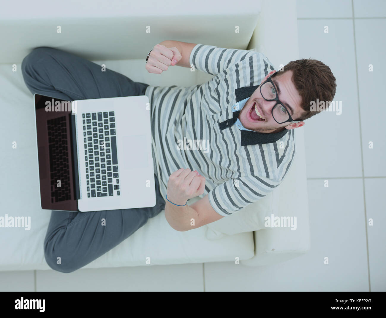 Top view of excited young man using his laptop in bright living room ...