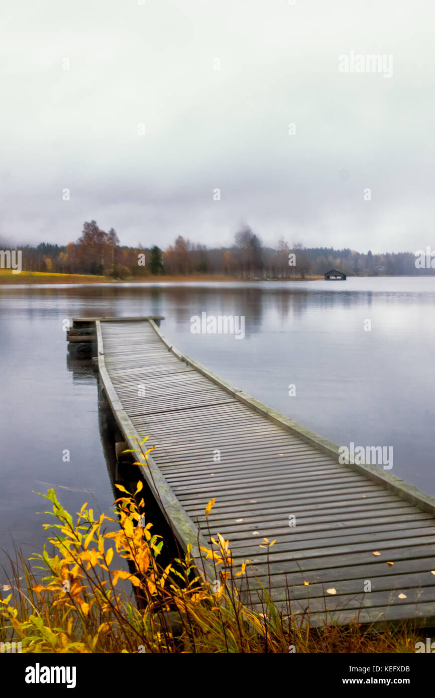 Autumn view of a lake in the Central Finland. A wooden pier provides a place for fishermen and boats. A lonely boat house is seen on the other side of Stock Photo