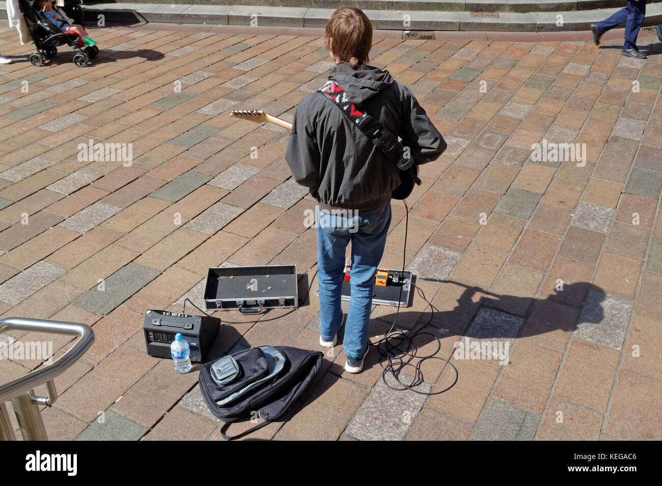 Glasgow music busker on street sidewalk placement   with guitar case shadow on a sunny day viewed from behind Stock Photo