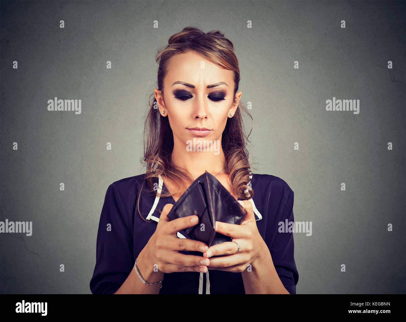 Worried young woman looking into her empty wallet Stock Photo