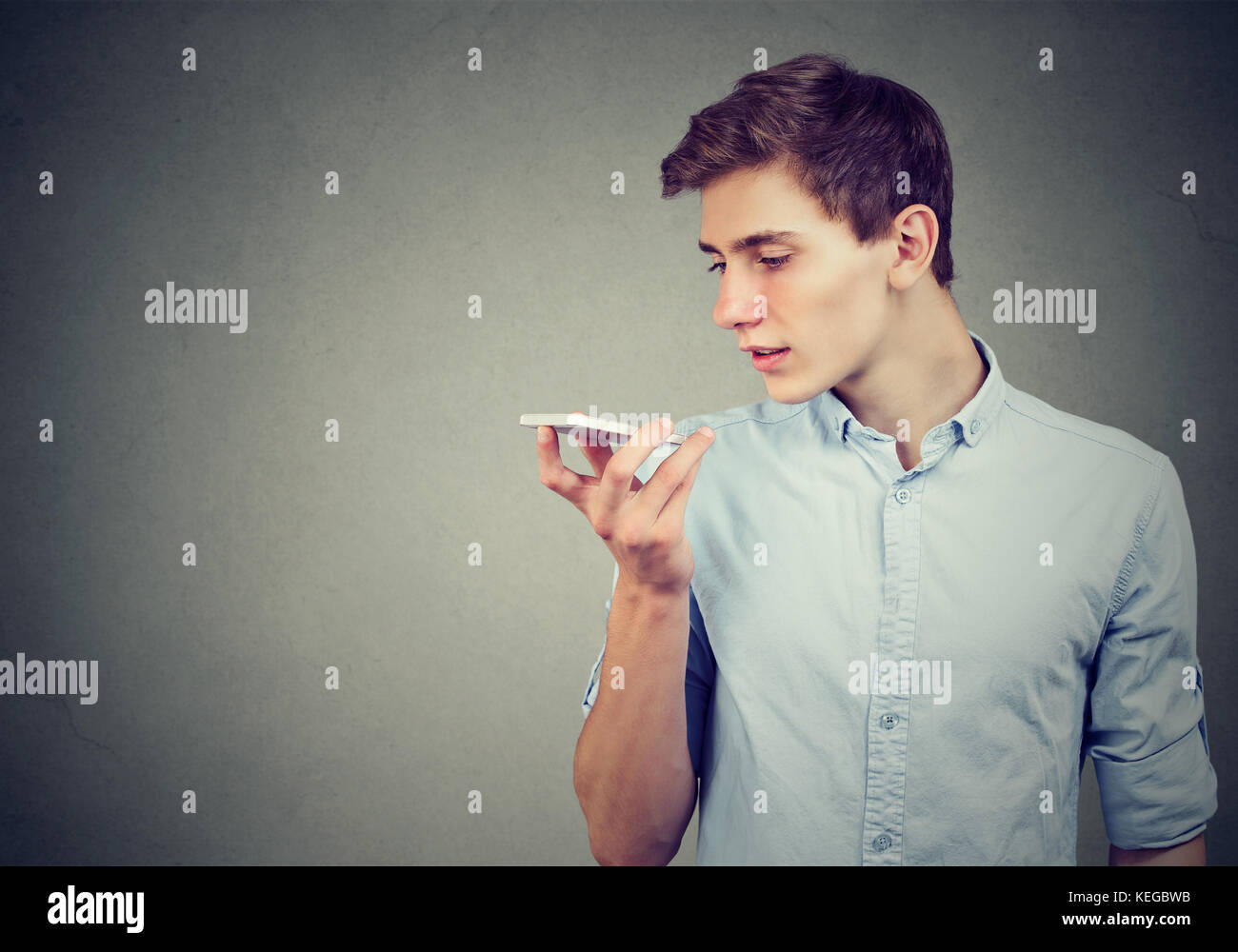 Young man using a smart phone voice recognition function isolated on gray wall background Stock Photo