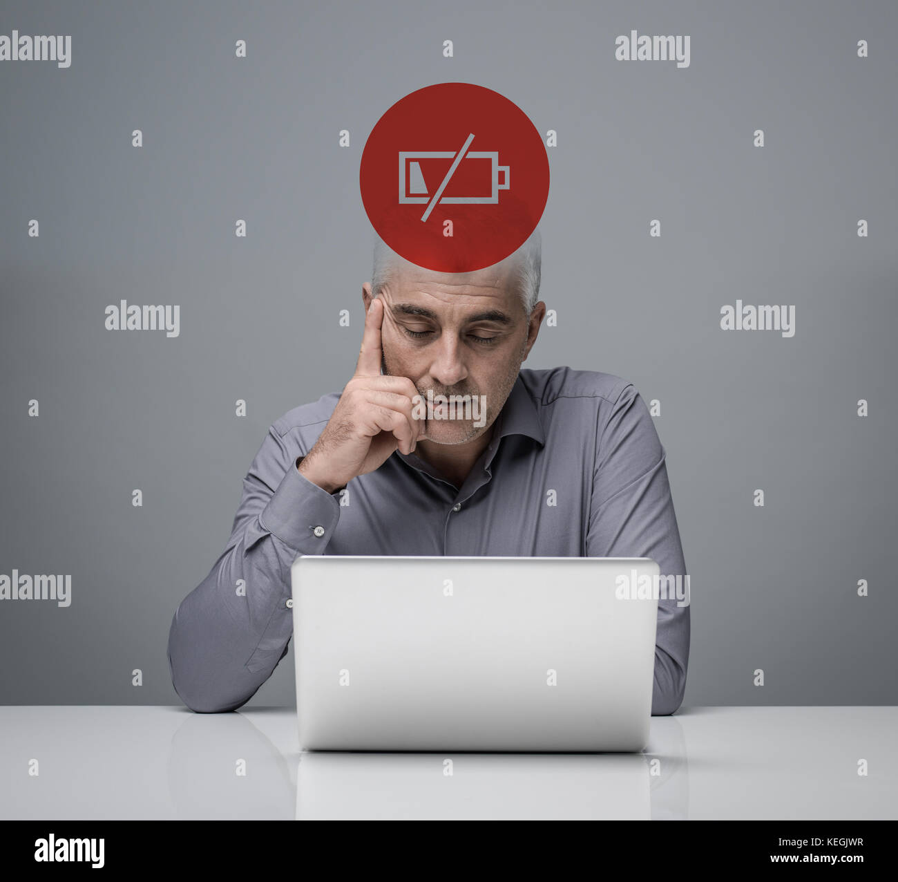 Tired businessman working with a laptop with low charge icon, stress and overwork concept Stock Photo