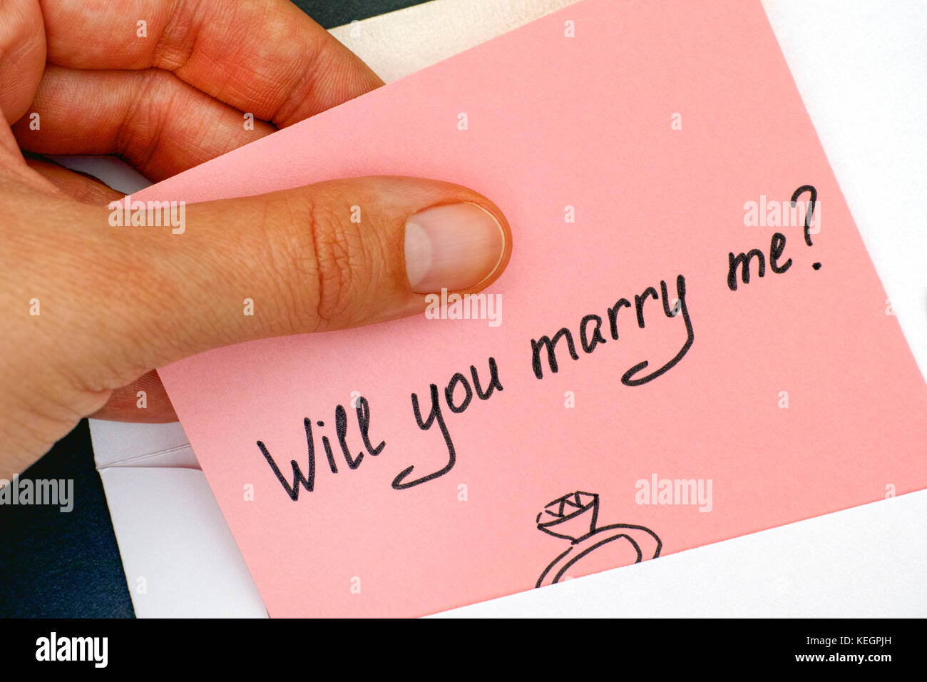 Woman hand taking out letter with text Will you marry me? from envelope. Close-up. Stock Photo