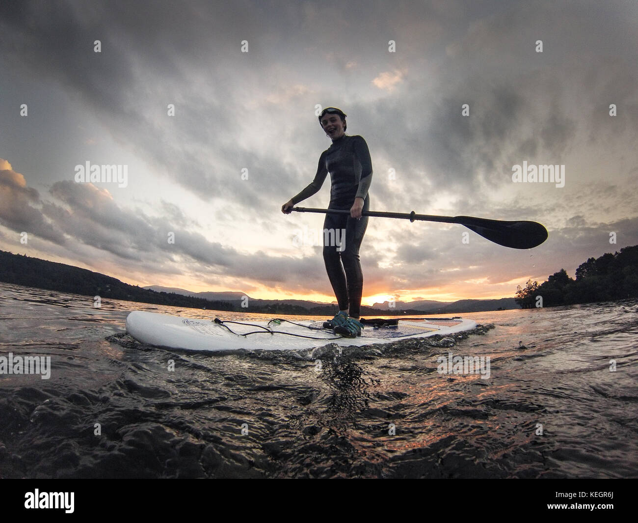 Girl paddle boarding on lake windermere Lake District as the sun sets