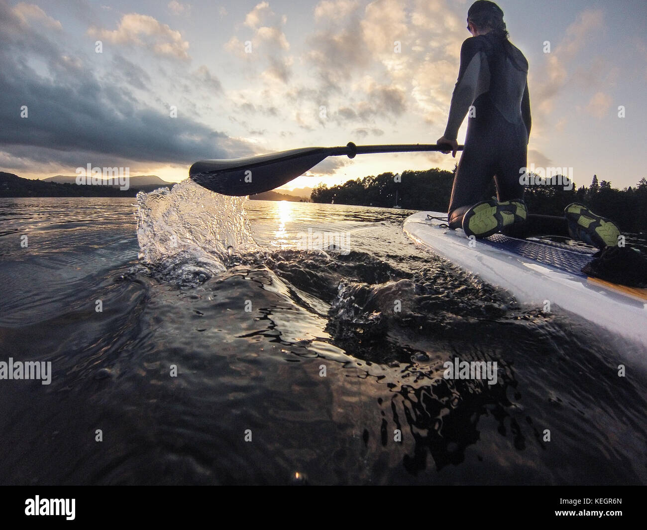 Girl paddle boarding on lake windermere Lake District as the sun sets