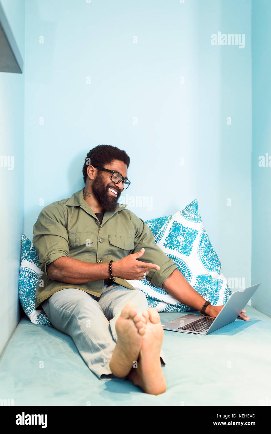 Smiling black man sitting on bed pointing at laptop Stock Photo Alamy