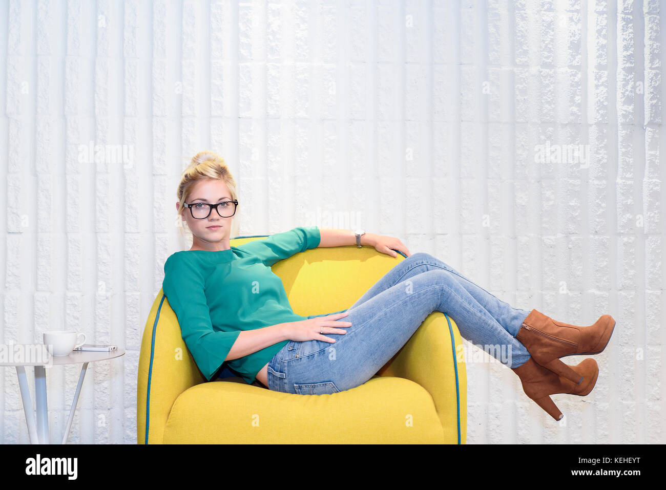 Serious Caucasian woman sitting in yellow chair Stock Photo