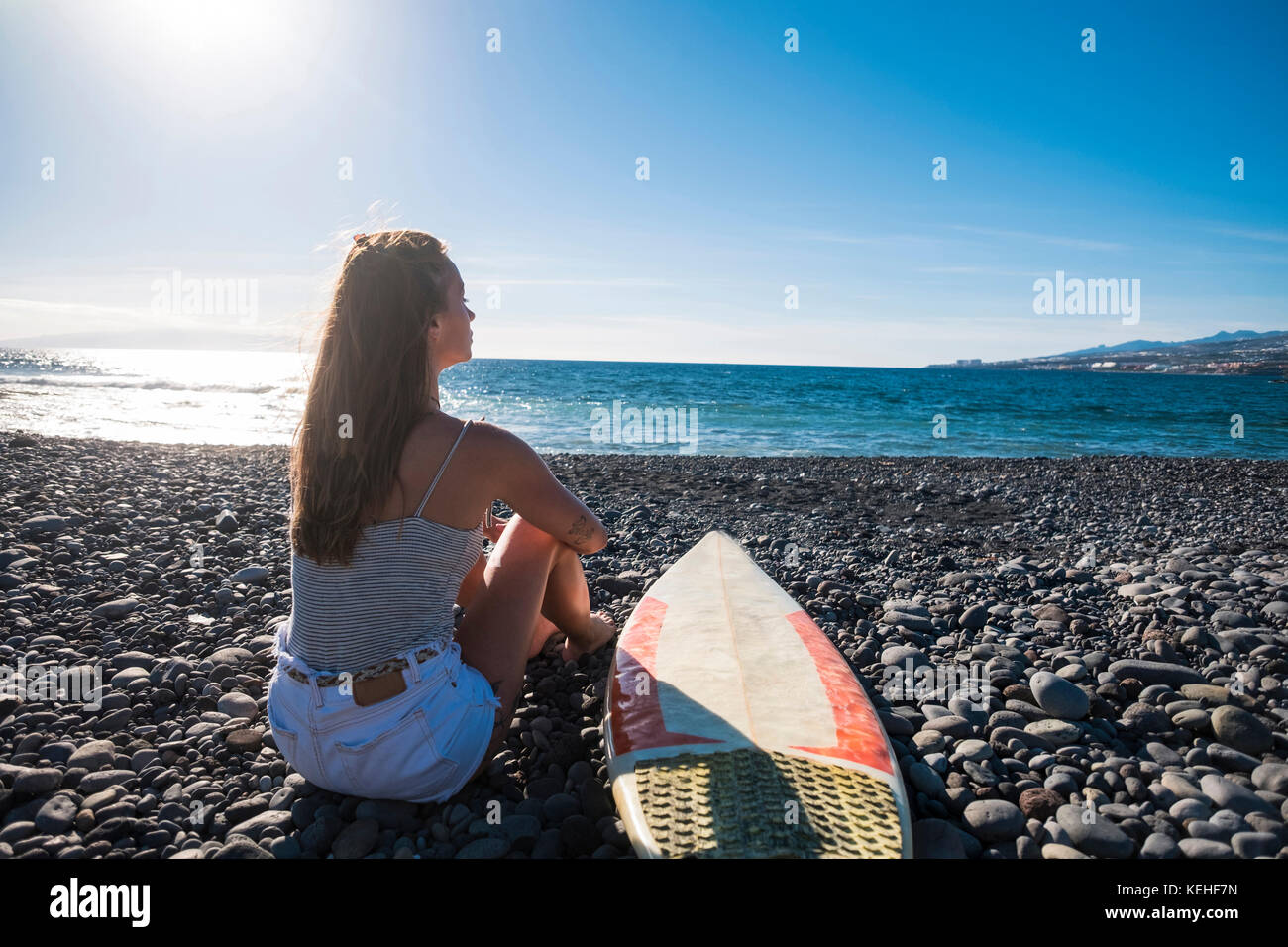 Caucasian woman sitting on beach near surfboard Stock Photo