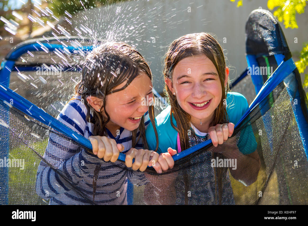 Water splashing on Caucasian girls leaning on netting Stock Photo