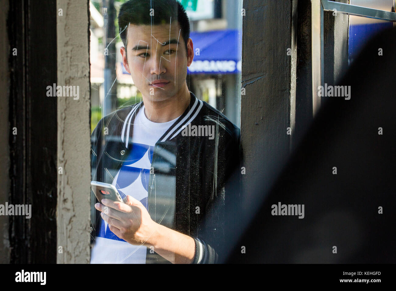 Serious Chinese man texting on cell phone behind window Stock Photo