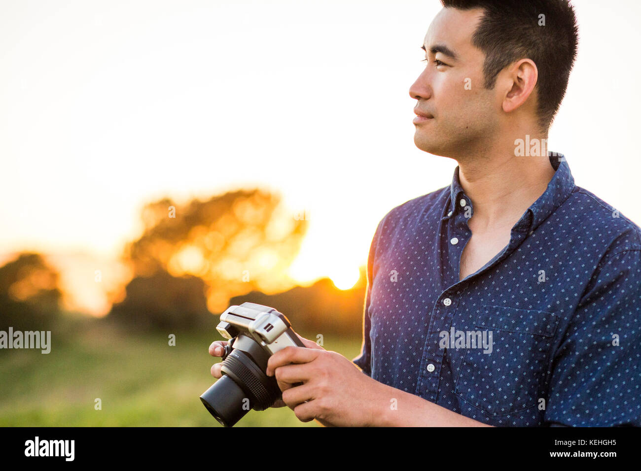 Smiling Chinese man holding camera in field Stock Photo