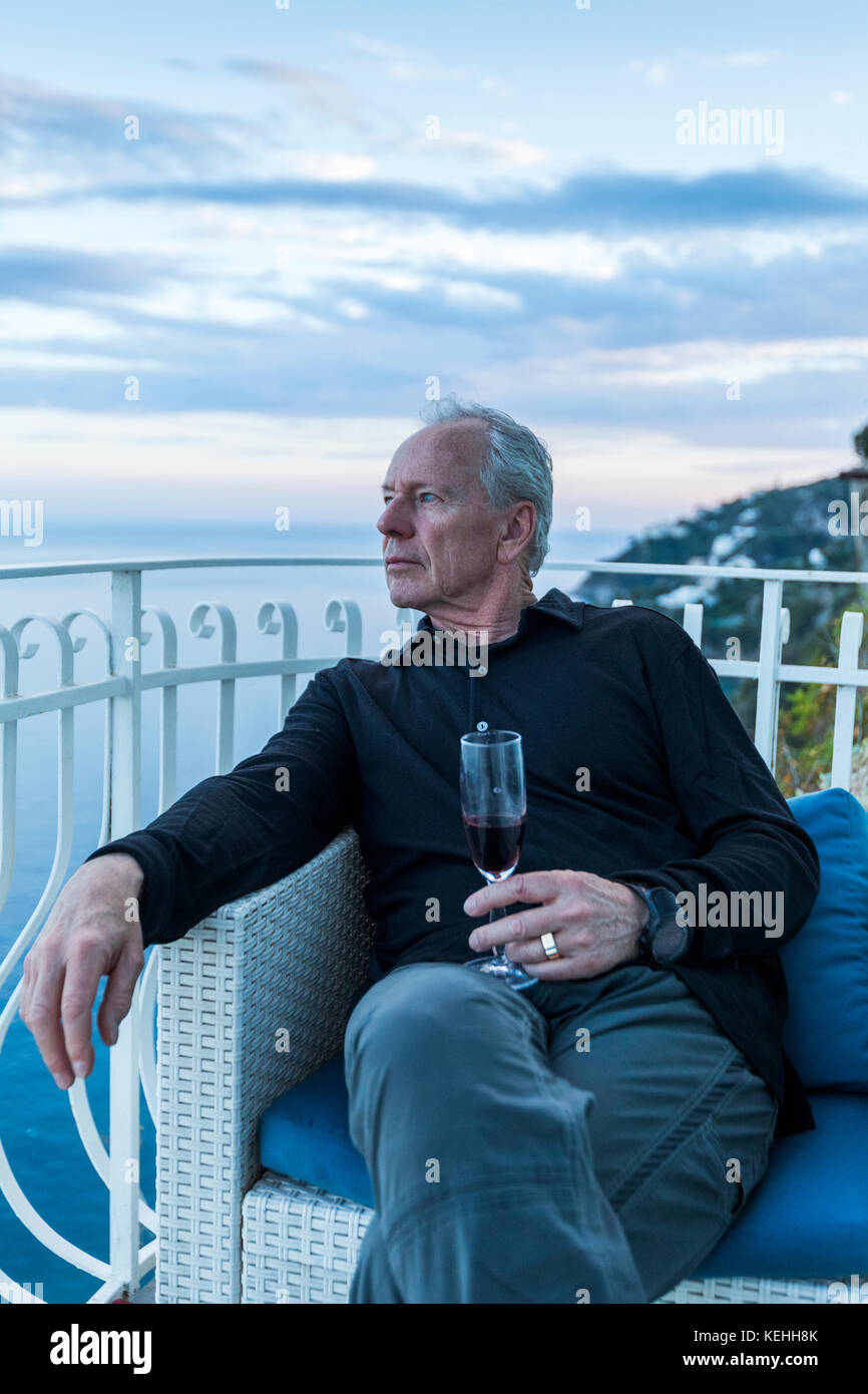 Caucasian man drinking wine on waterfront balcony Stock Photo
