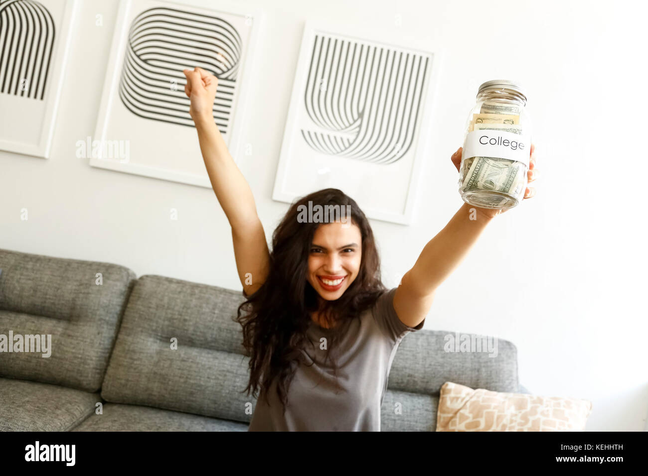 Mixed race woman on sofa celebrating with college money Stock Photo