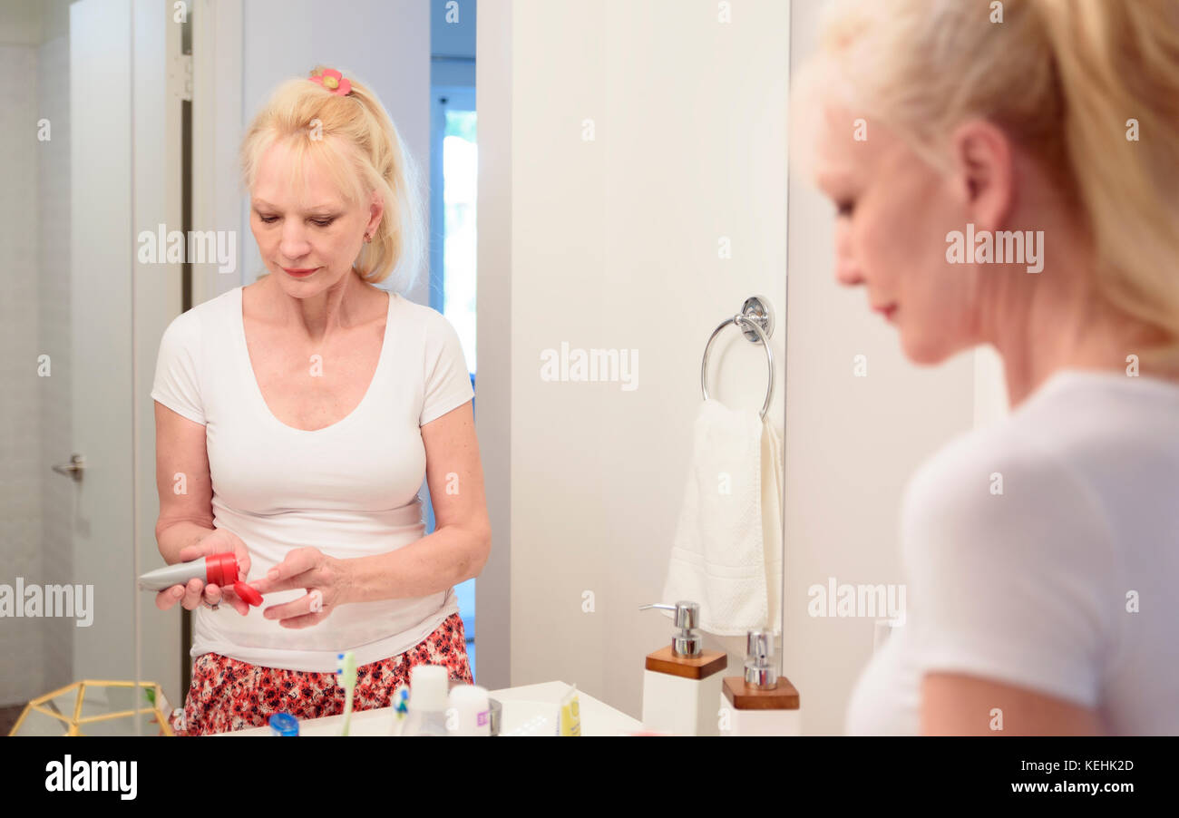 Caucasian woman squeezing lotion onto finger in mirror Stock Photo