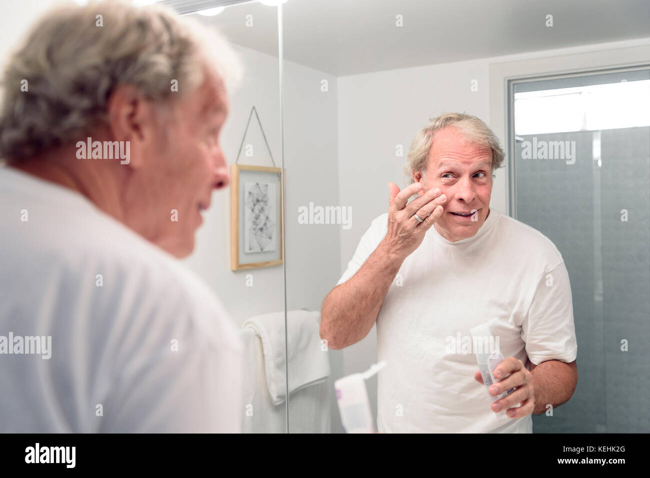 Caucasian man applying lotion to face in mirror Stock Photo