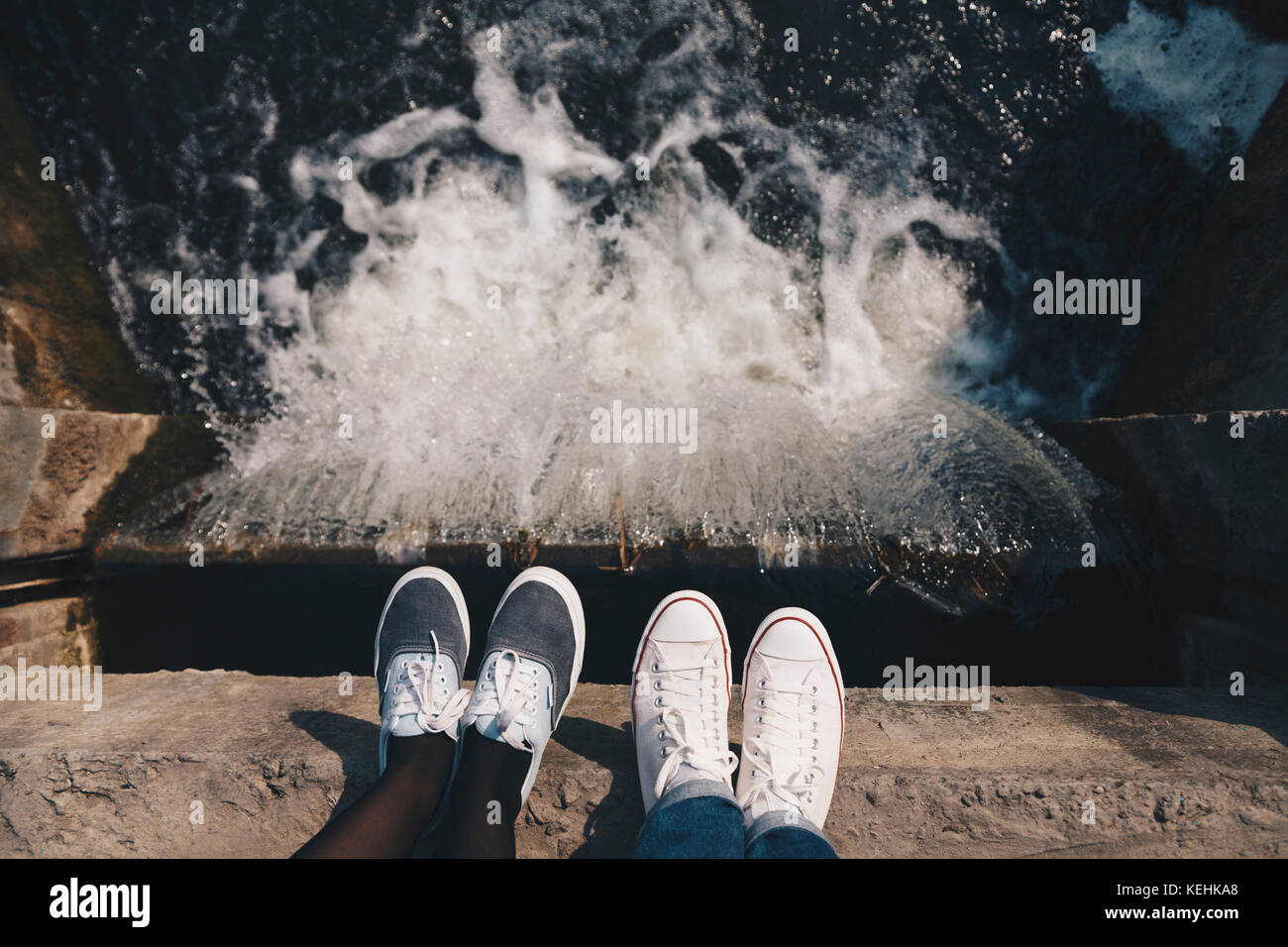 Feet of people standing at the edge of flowing water Stock Photo