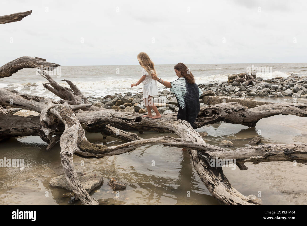 Caucasian mother and daughter walking on driftwood on beach Stock Photo