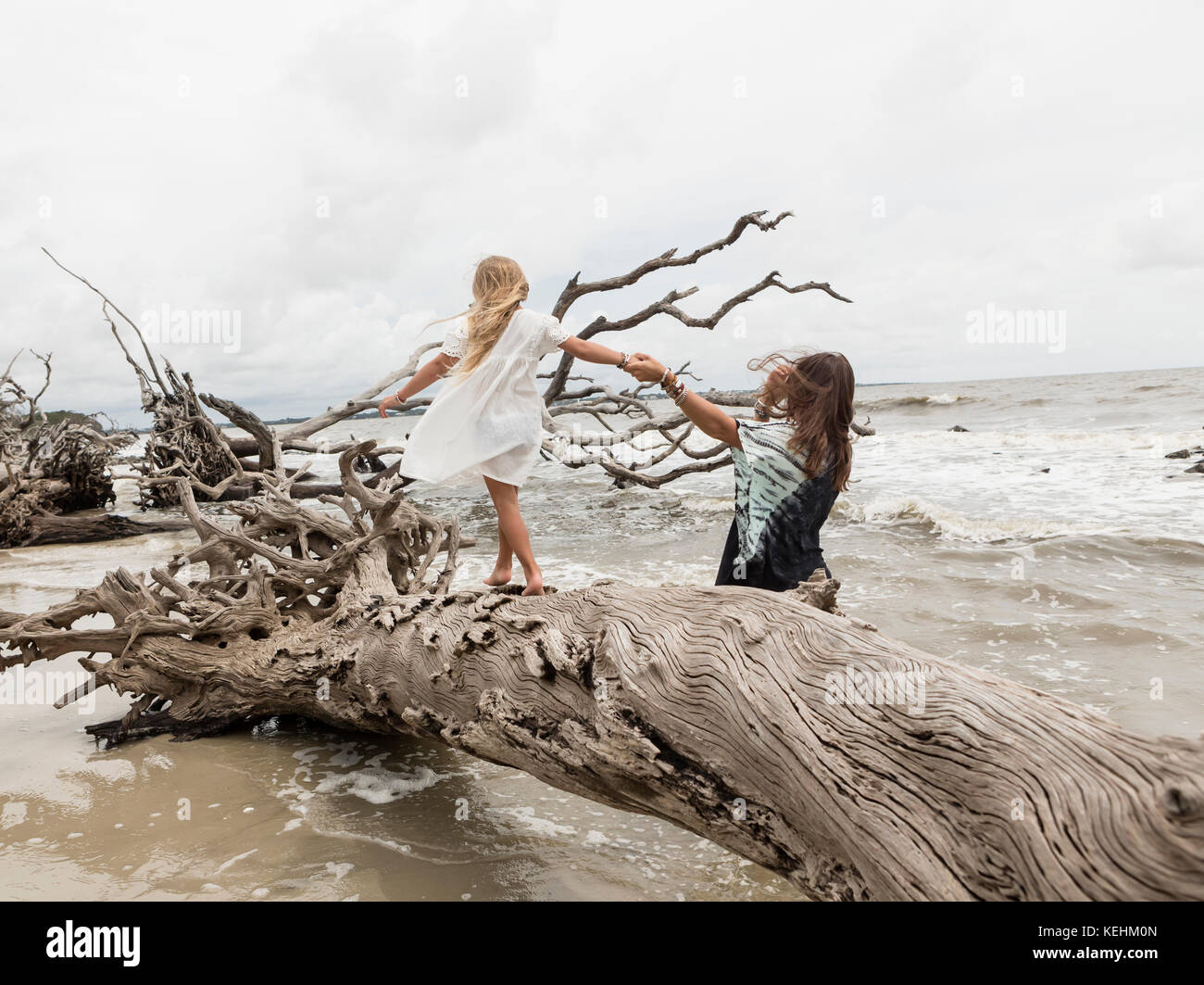 Caucasian mother and daughter walking on driftwood on beach Stock Photo