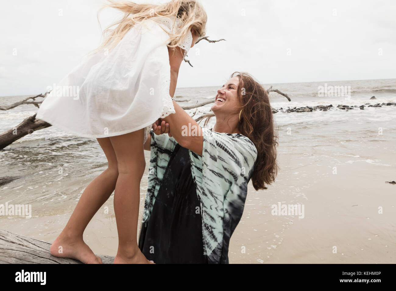 Caucasian mother and daughter playing on driftwood on beach Stock Photo
