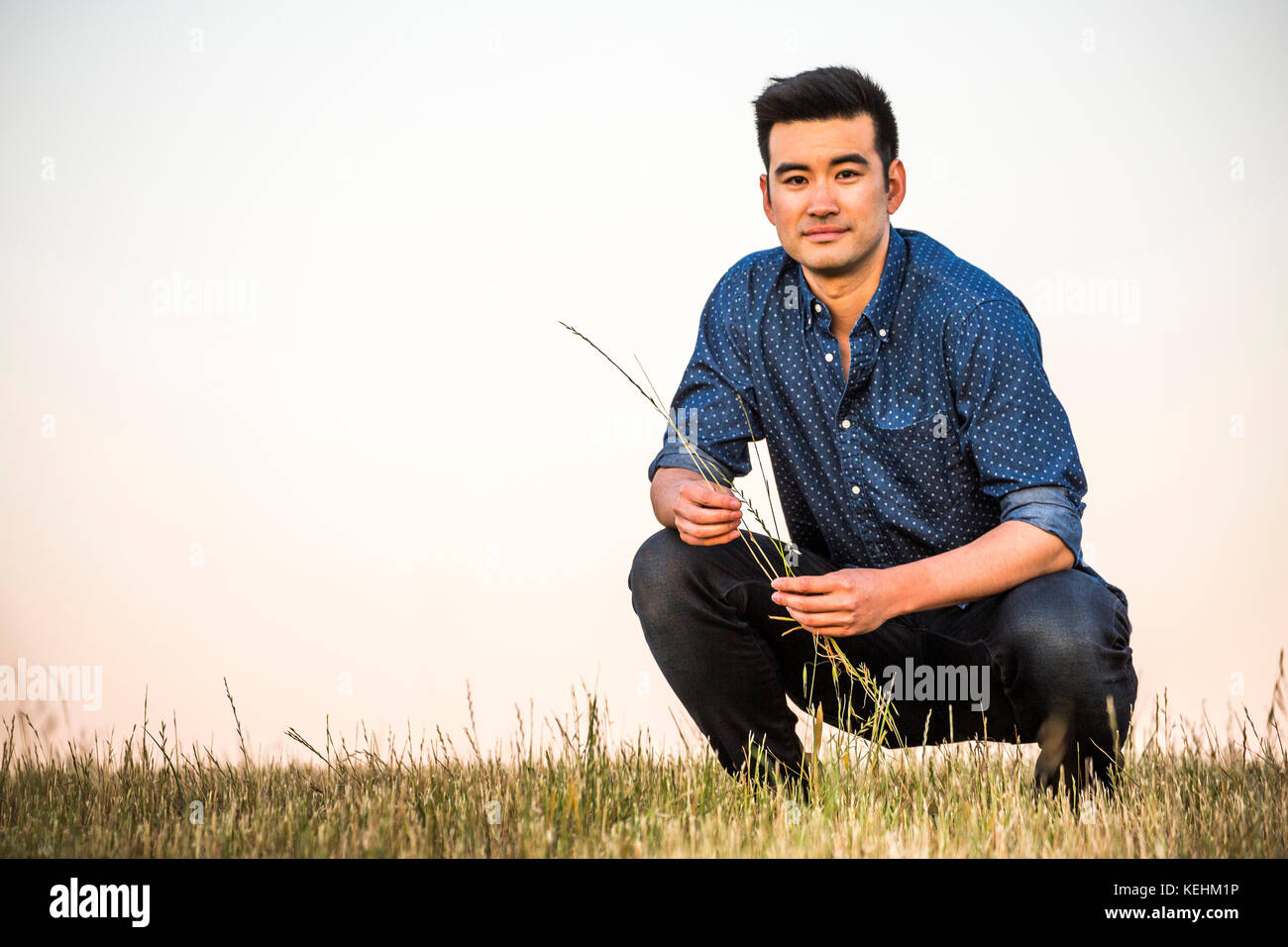 Chinese man crouching in field holding grass Stock Photo