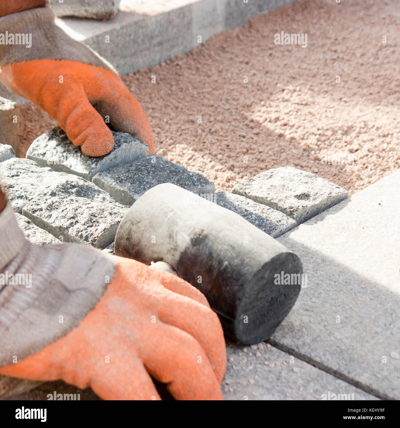 Hands in gloves of a builder worker laying on the granite cobblestone sett  on sand with rubber mallet , and paving street sidewalk on construction si Stock Photo