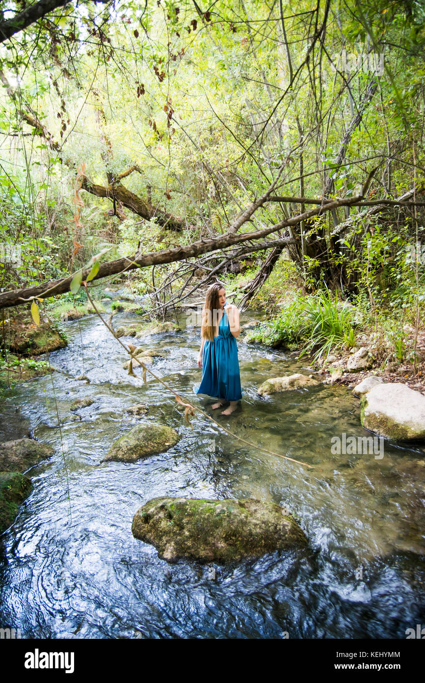 Beautiful woman on the bank of a mountain river with an evening dress ...