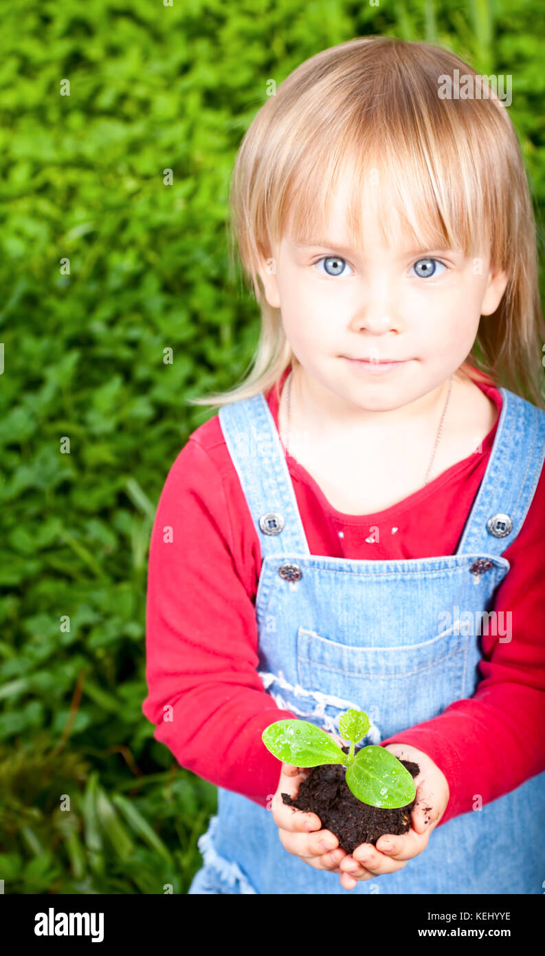 Blonde girl wearing red dress showing seeding with ground, focus on sprout Stock Photo