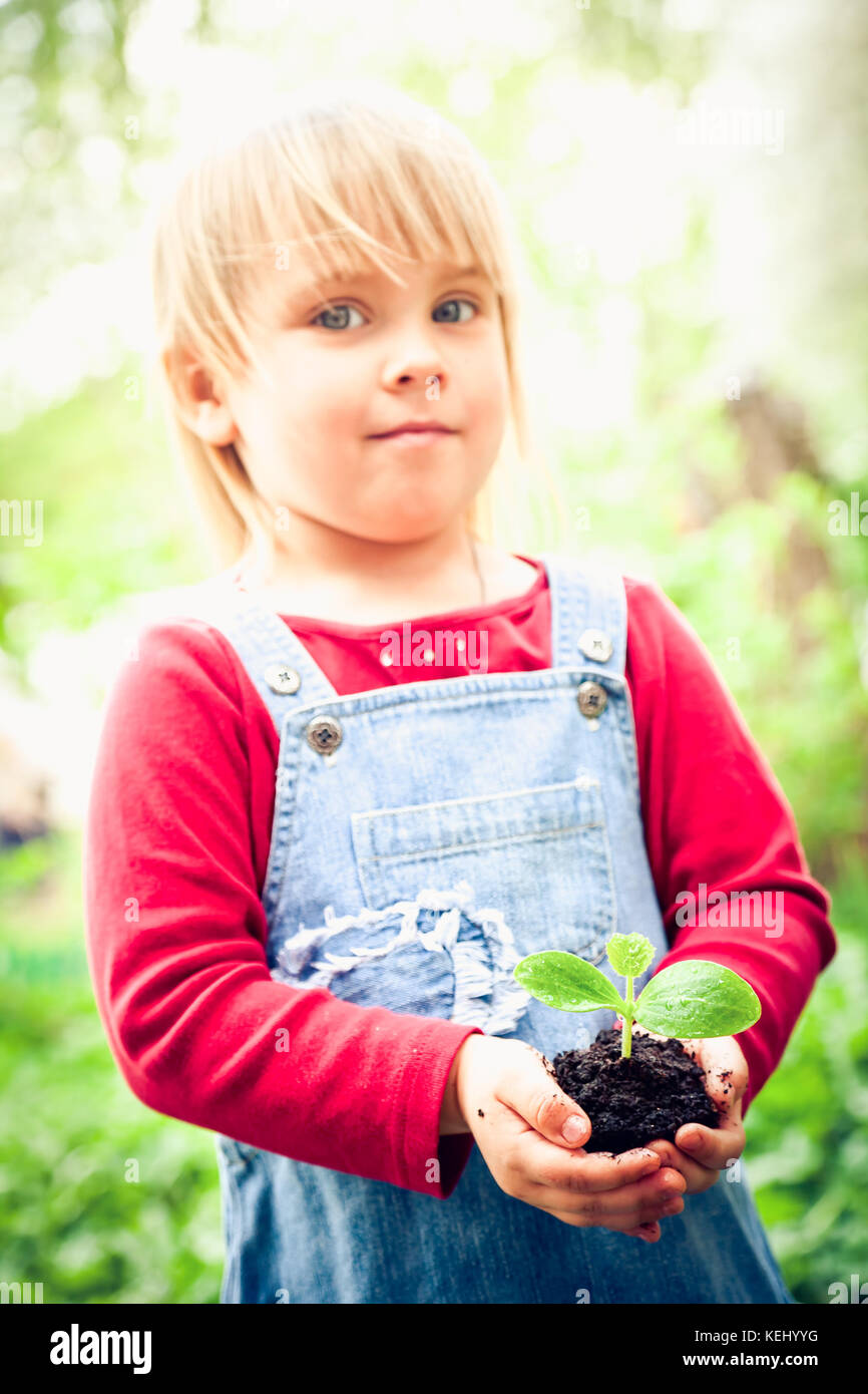 Blonde girl wearing red dress showing seeding with ground, focus on sprout Stock Photo