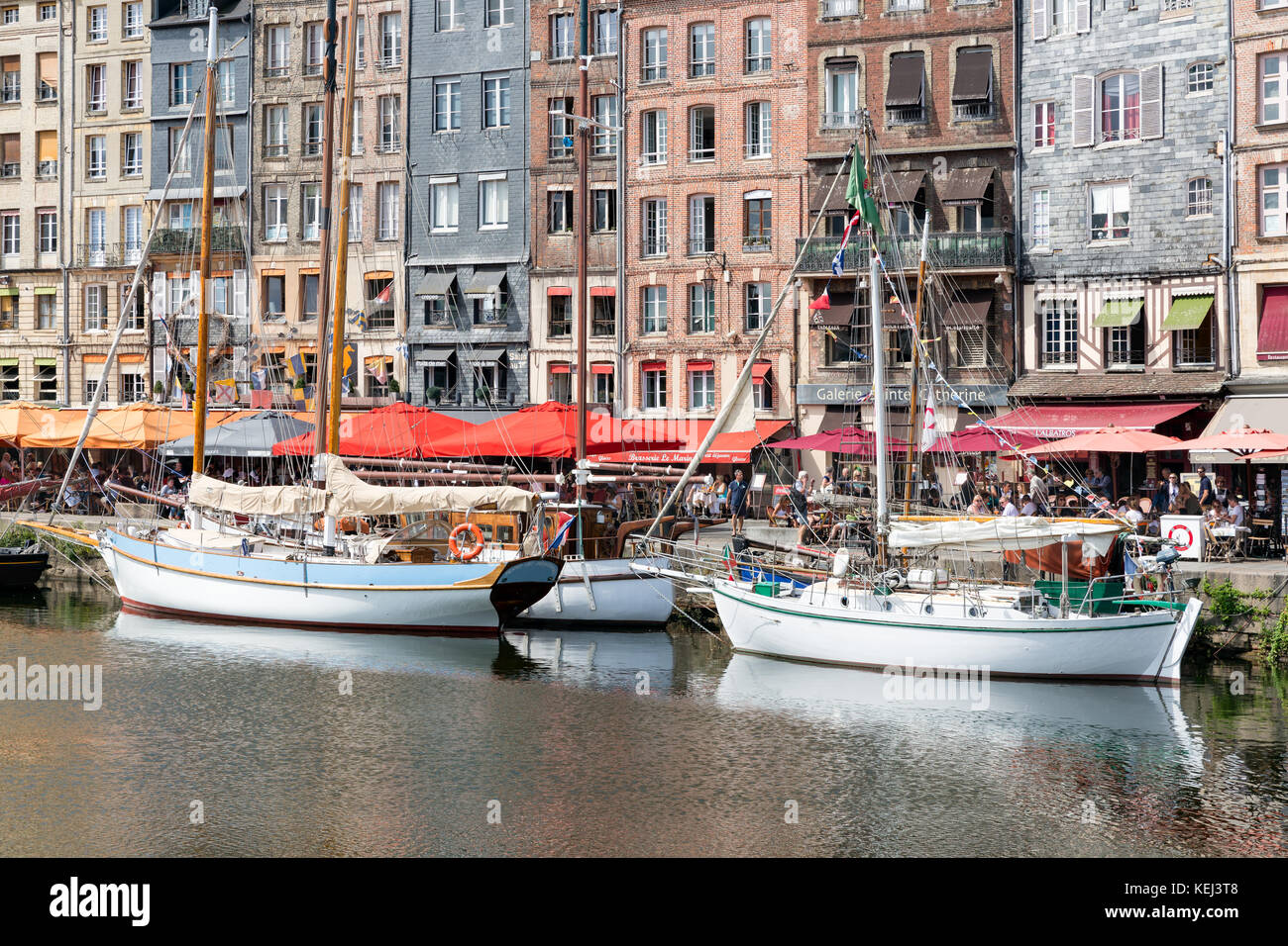 HONFLEUR, FRANCE - AUGUST 24, 2017: Harbor of historic city Honfleur with moord sailing ships. Many tourists enjoy the sunny weather and take a lunch  Stock Photo