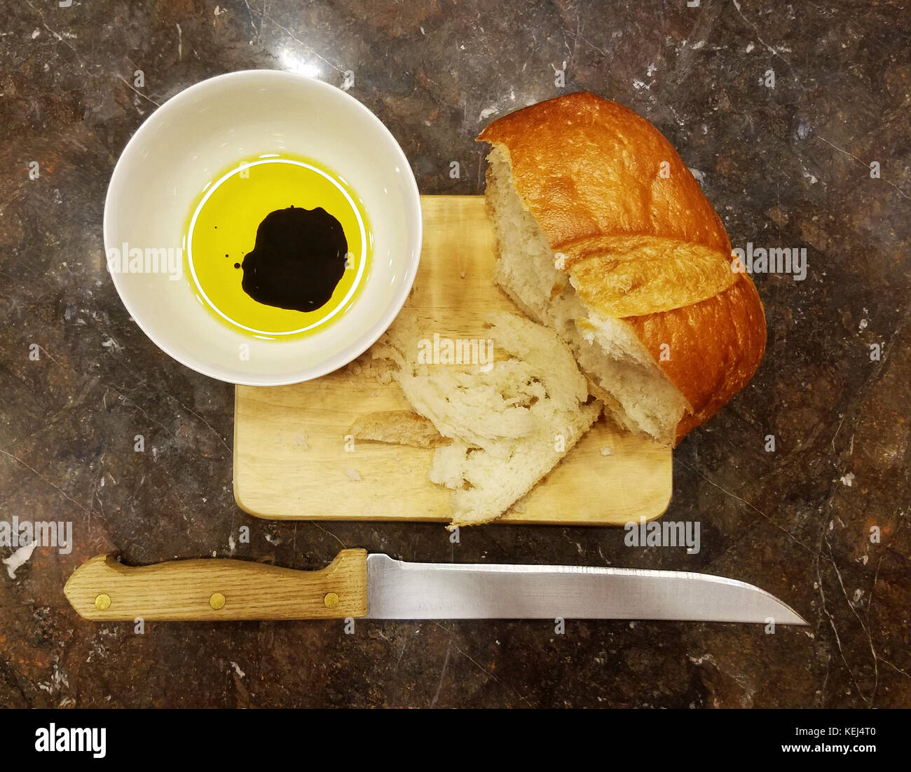 A cutting board with bread, olive oil, and vinegar with a bread knife Stock Photo