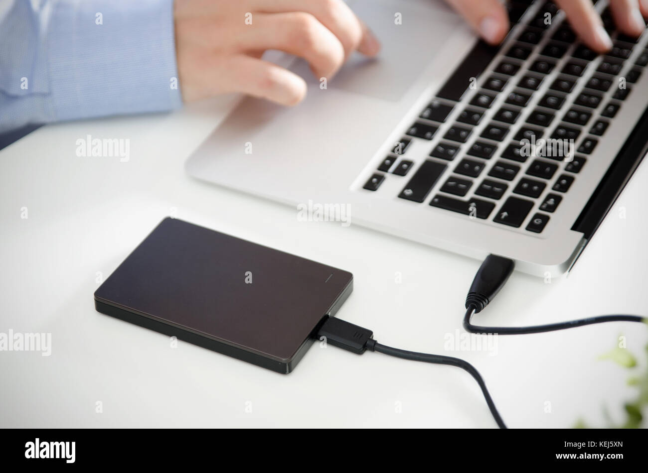 External backup disk hard drive connected to laptop. Man with notebook making safety personal data copy. Stock Photo