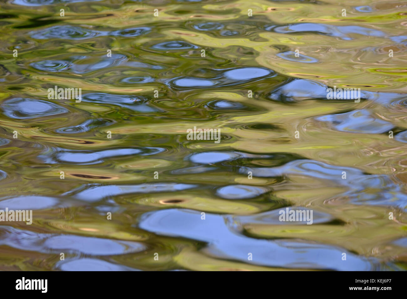 Abstract swirling pattern formed by sky and trees reflected in the surface of rippling water Stock Photo